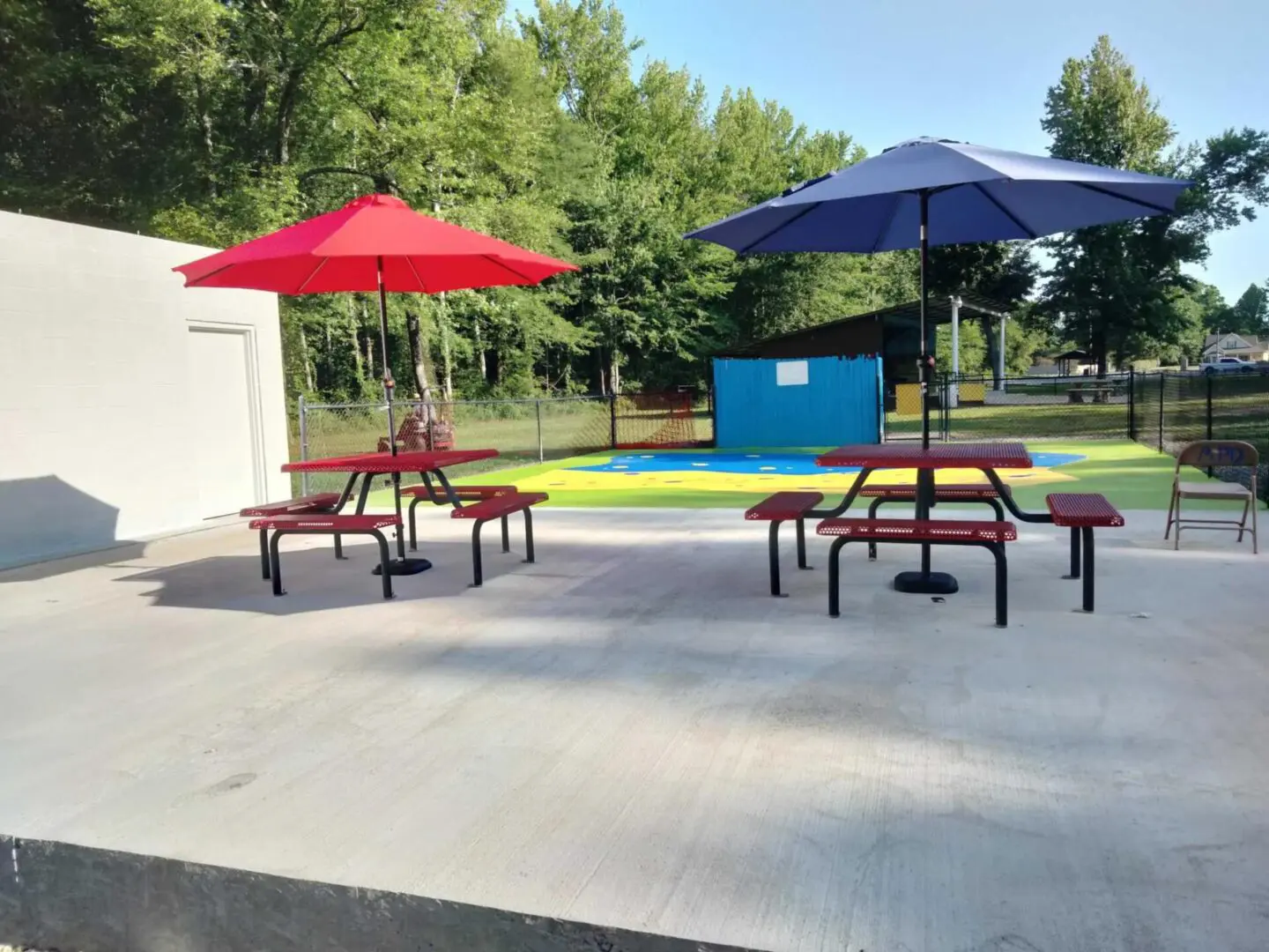A picnic table with two umbrellas and one bench.
